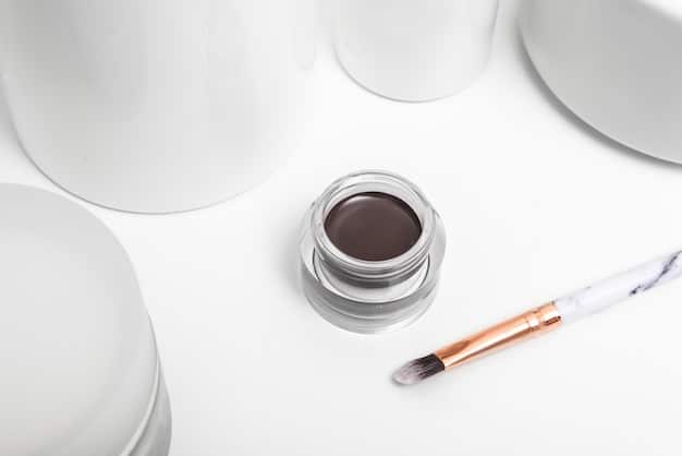 A close-up shot of various minimalist makeup products, including a tinted moisturizer, brow gel, cream blush, and lip balm, arranged neatly on a white marble surface.