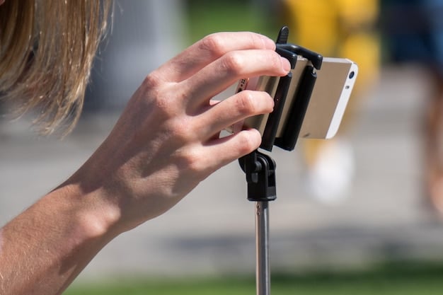 A close-up of a journalist's hands operating a smartphone mounted on a compact gimbal, with an external microphone attached. The scene suggests a focused and professional approach to mobile videography, perhaps during an interview or field reporting.